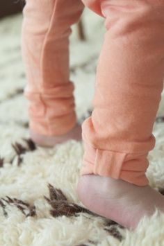 a close up of a child's feet wearing pink pants and shoes on a rug