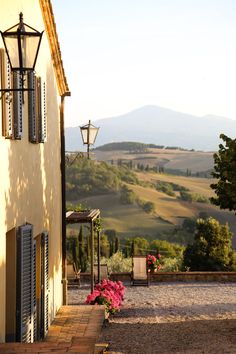 an outside view of a house with flowers in the foreground and mountains in the background