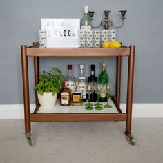 a bar cart with liquor bottles and glasses on it, sitting next to a potted plant