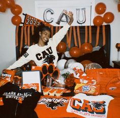 a woman sitting on top of a bed surrounded by orange and white balloons, decorations and gifts