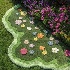 a green rug with flowers on it in the middle of some grass and purple flowers