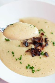 a spoon full of soup with bacon and parsley on top in a white bowl