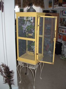 a yellow cabinet sitting in the corner of a room next to a vase with flowers