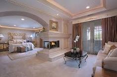 a large bedroom with a fireplace in the center and white carpeted flooring on the other side