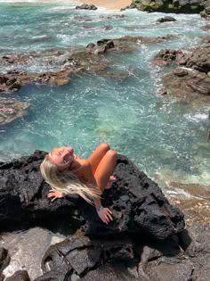 a woman laying on top of a rock next to the ocean