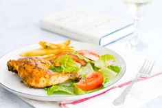 a white plate topped with chicken, lettuce and tomatoes next to a glass of wine