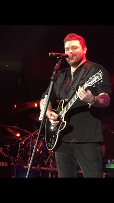 a man standing in front of a microphone while holding a guitar