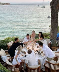 a group of people sitting around a table with food and drinks in front of the water