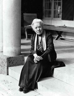 an old woman sitting on the steps in front of a building with columns and benches