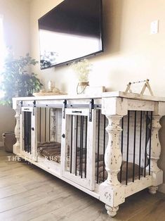 a white dog kennel in the corner of a room with wood floors and a flat screen tv mounted on the wall