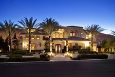 a large house lit up at night with palm trees in the front yard and landscaping