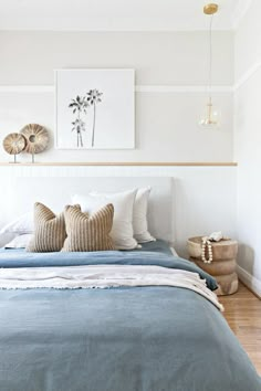 a bed with blue sheets and pillows in a bedroom next to a painting on the wall