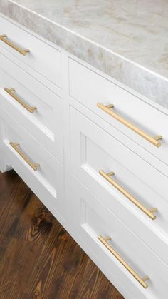 a kitchen counter with white cabinets and gold pulls on it's doors, in front of a wood floor