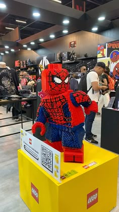 a lego spider man is on display in a store, with people looking at it