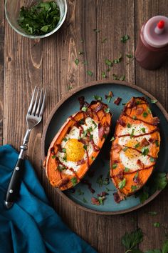 two baked sweet potatoes with bacon and eggs on a plate next to a fork, glass of juice and napkin