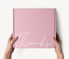 two hands holding a pink thank card with the word thanks written on it in white ink