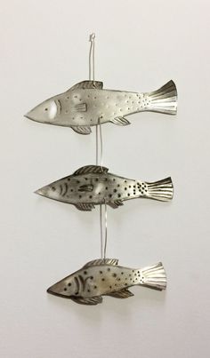 three metal fish hanging from strings on a wall in the shape of an ornament