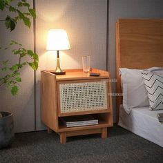 a night stand with a lamp on it next to a bed and a potted plant