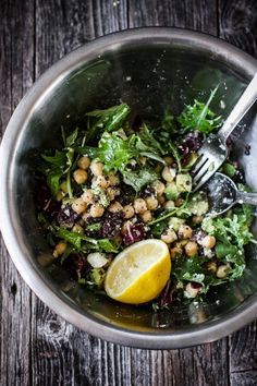 a salad in a bowl with lemon wedges on the side