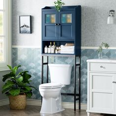 a white toilet sitting in a bathroom next to a blue cabinet and potted plant