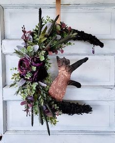 a wreath made out of fake flowers and leaves hangs on a door with a cat