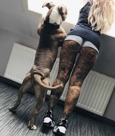 a woman standing next to a dog with tattoos on her legs and leggings