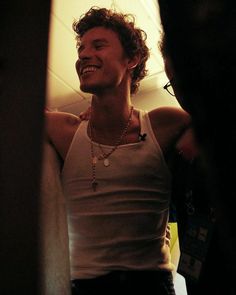 a man with curly hair is smiling and wearing a white tank top while standing in front of a mirror