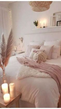 a white bed with pillows and blankets on top of it next to two lit candles