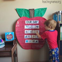 a young child is writing on an apple shaped bulletin board