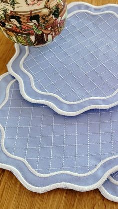 three blue placemats with white trim on them sitting on a wooden table next to a bowl