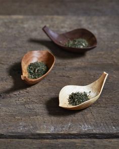 two wooden spoons filled with green tea on top of a wooden table next to each other