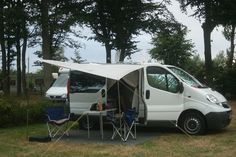 a camper van is parked in the grass with its door open and it's awning opened