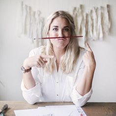 a woman sitting at a table with a pencil in her mouth