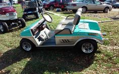 an electric golf cart is parked on the grass in front of other cars and trucks