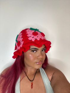 a woman with long red hair wearing a crocheted strawberry hat and tank top