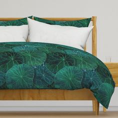 a bed with green leaves on it and two pillows in front of the headboard