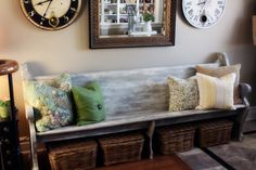 a wooden bench with baskets underneath it in front of a mirror and clock on the wall