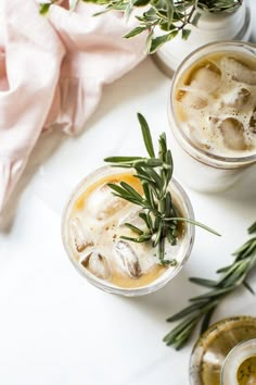 two glasses filled with drinks sitting on top of a white table next to green leaves