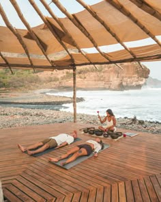 two people are doing yoga on a wooden deck near the water and rocks in the background