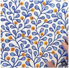 someone is drawing on a wall with blue and orange flowers in the background, while holding a pen