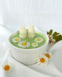 two little bunnies sitting in a bowl of green liquid with daisies on the side