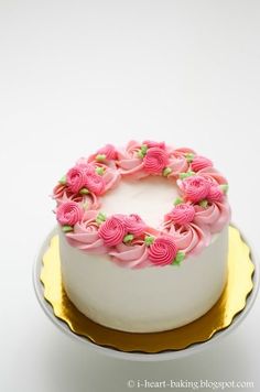 a white cake with pink frosting and roses on top is sitting on a gold plate