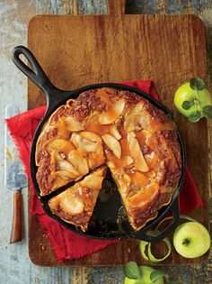 an apple pie with slices cut out on a wooden cutting board next to green apples