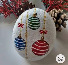 an egg decorated with christmas ornaments next to pine cones