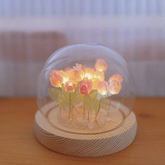 there is a glass ball with flowers in it on a wooden base and some lights inside