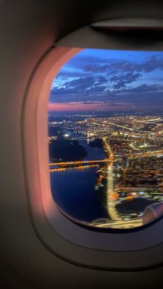 an airplane window with the view of a city and water at night from inside it