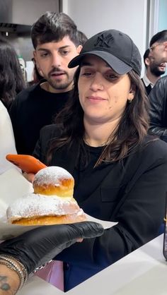 a woman holding up a donut covered in powdered sugar and an orange carrot