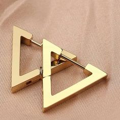 a pair of triangle shaped earrings on top of a pink cloth with gold colored metal fittings