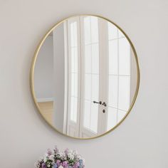 a round mirror on the wall above a table with flowers and vase in front of it