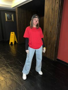 a woman in red shirt and blue pants standing on black floor next to yellow caution sign